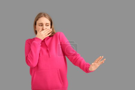 Young woman feeling terrible smell on grey background