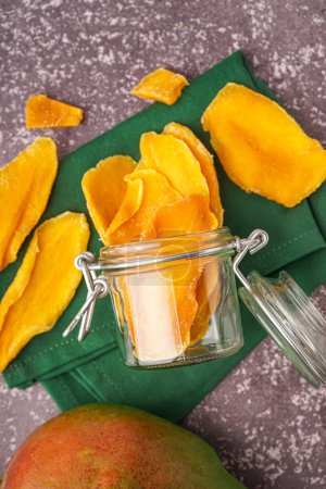 Jar with slices of dried mango on dark table