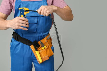Male electrician with wire and crimper on grey background, closeup