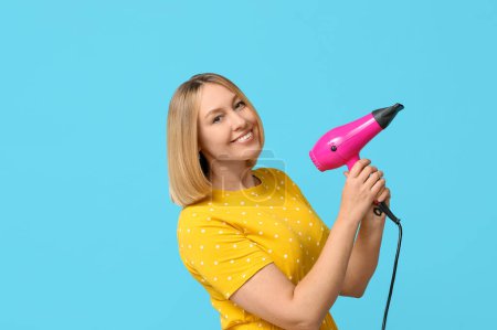 Beautiful young woman with bob hairstyle holding hair dryer on blue background