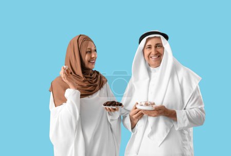 Happy Muslim couple with traditional sweets on blue background. Eid al-Fitr celebration