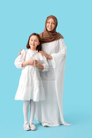 Glückliche muslimische Mutter mit ihrer Tochter auf blauem Hintergrund. Eid al-Fitr-Feier