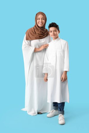 Happy Muslim mother with her son on blue background. Eid al-Fitr celebration
