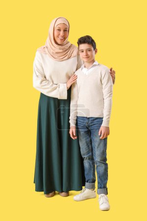 Happy Muslim mother and her son on yellow background. Eid al-Fitr celebration