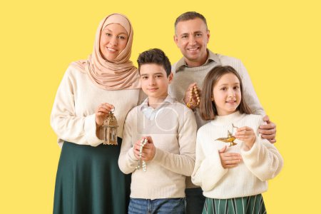 Happy Muslim family with traditional accessories on yellow background. Eid al-Fitr celebration