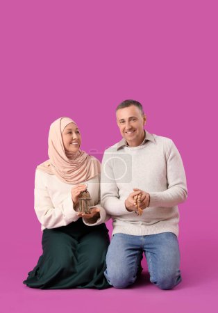 Happy Muslim couple with prayer beads and fanoos on pink background. Eid al-Fitr celebration