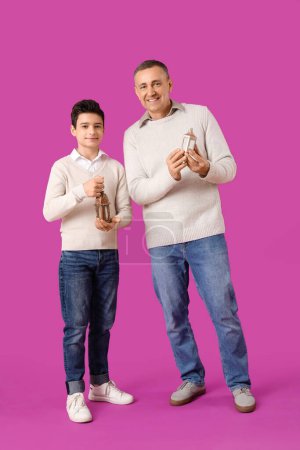 Happy Muslim father and his son with fanoos on pink background. Eid al-Fitr celebration