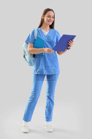 Female medical intern with clipboard on light background