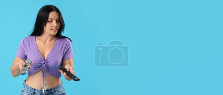 Nachdenkliche junge Frau mit Fernbedienungen auf blauem Hintergrund mit Platz für Text