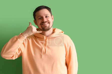 Photo for Handsome man showing "call me" gesture on green background - Royalty Free Image