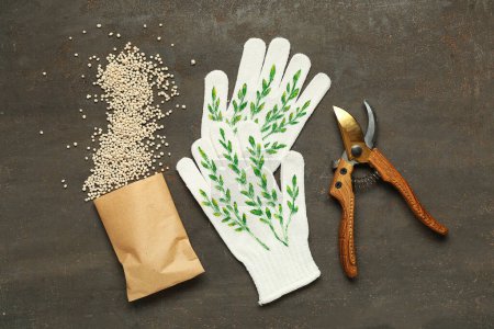 Granular fertilizer, gloves and gardening pruner on grey grunge background
