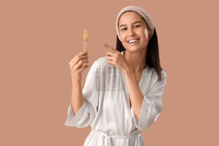 Photo for Beautiful young happy woman pointing at spatula with sugaring paste on brown background - Royalty Free Image