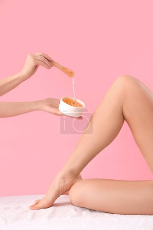 Beautician depilación piernas de hermosa mujer joven con pasta de azúcar sobre fondo rosa