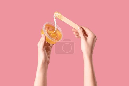 Main féminine tenant le récipient avec de la pâte à sucre et de la spatule sur fond rose