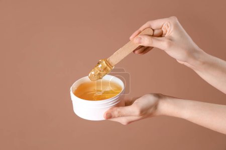 Photo for Female hands holding container with sugaring paste and spatula on brown background - Royalty Free Image
