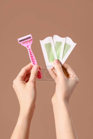 Photo for Female hands with razor and wax strips on brown background - Royalty Free Image