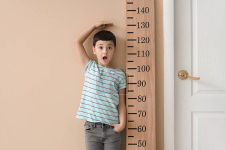 Shocked little boy measuring height near wooden stadiometer