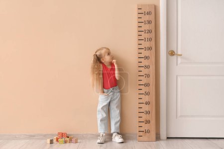 Thoughtful little girl measuring height near wooden stadiometer