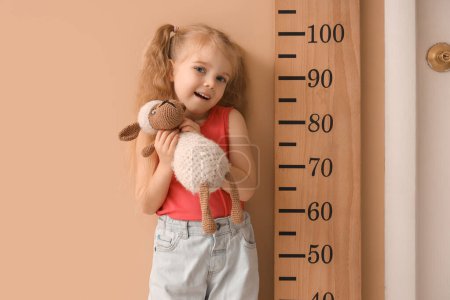Cute little girl with plush toy measuring height near wooden stadiometer