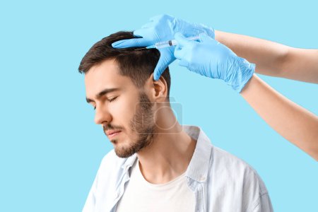 Photo for Young brunette man receiving injection for hair growth on blue background, closeup - Royalty Free Image