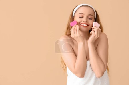 Beautiful young woman with heart-shaped sponges on beige background