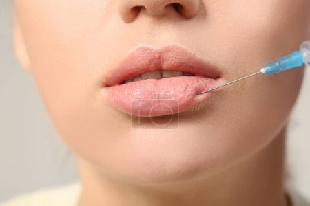 Young woman receiving lip injection against grey background, closeup