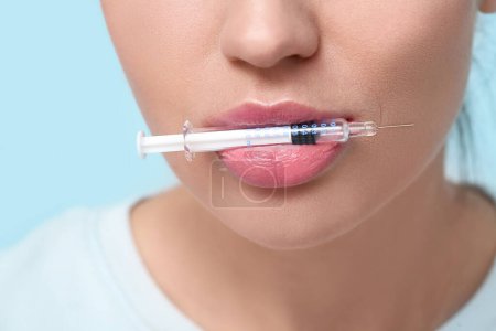 Junge Frau hält Injektionsspritze im Mund auf farbigem Hintergrund, Nahaufnahme