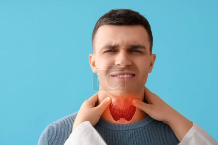 Endocrinologist examining thyroid gland of young man on blue background