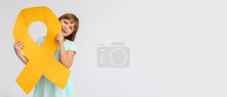 Téléchargez les photos : Petite fille tenant un grand ruban doré sur fond clair avec de l'espace pour le texte. Concept de sensibilisation au cancer chez l'enfant - en image libre de droit