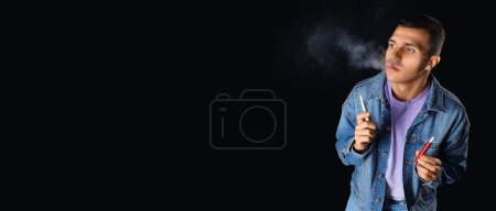 Téléchargez les photos : Jeune homme fumant des cigarettes électroniques sur fond noir avec espace pour le texte - en image libre de droit