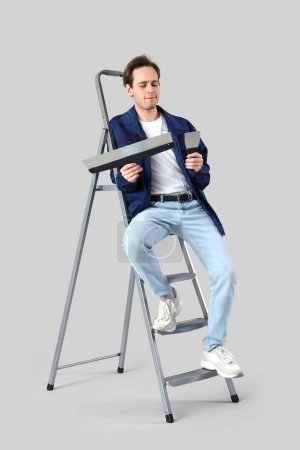 Young man with putty knives and stepladder on light background