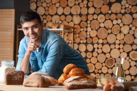 Photo for Young man with loaves of fresh bread at table in bakery - Royalty Free Image