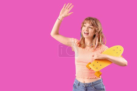 Young woman with skateboard waving hand on purple background
