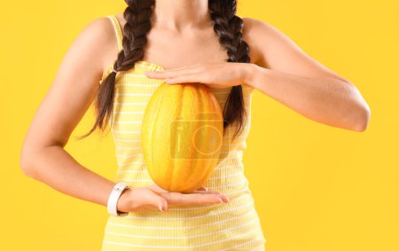 Beautiful young Asian woman with whole fresh melon on yellow background, closeup