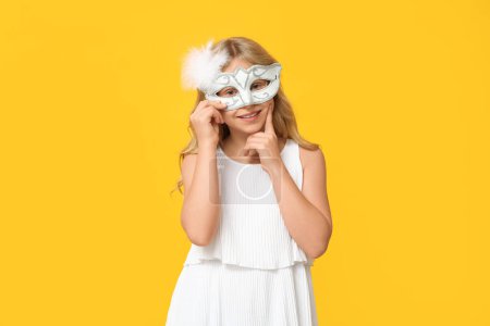Photo for Thoughtful little girl wearing carnival mask on yellow background - Royalty Free Image