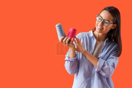 Photo for Female tailor in eyeglasses with thread spools on orange background - Royalty Free Image