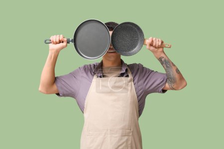 Photo for Portrait of handsome young man covering face with frying pans on green background - Royalty Free Image