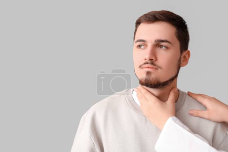 Endocrinologist examining thyroid gland of young man on grey background