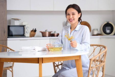 Junge Asiatin bereitet Dampf-Inhalation mit Kräutern am Tisch in Küche zu