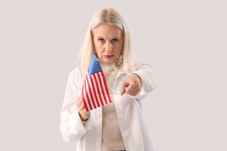 Reife Frau mit USA-Fahne, die auf den Betrachter auf hellem Hintergrund zeigt. Anschuldigungskonzept