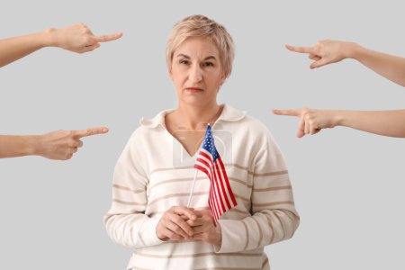 Menschen zeigen auf eine reife Frau mit US-Flagge auf hellem Hintergrund. Anschuldigungskonzept