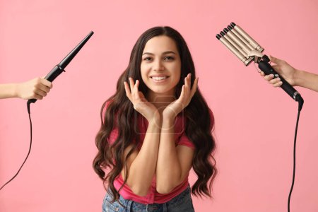 Téléchargez les photos : Belle jeune femme et les mains avec différents fers à friser sur fond rose - en image libre de droit
