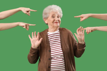Menschen zeigen auf eine Seniorin auf grünem Hintergrund. Anschuldigungskonzept