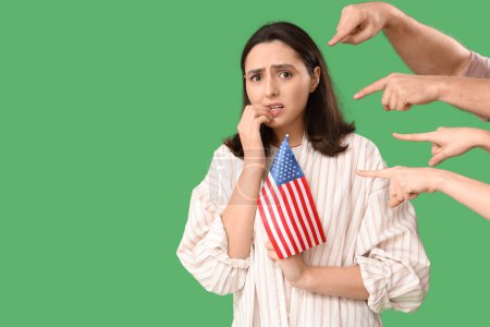 Menschen zeigen auf eine besorgte junge Frau mit US-Flagge auf grünem Hintergrund. Anschuldigungskonzept
