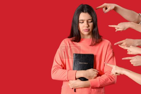 Foto de Gente señalando a una joven con la Sagrada Biblia sobre fondo rojo. Concepto de acusación - Imagen libre de derechos
