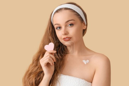 Beautiful young woman with heart made of cream and sponge on beige background, closeup