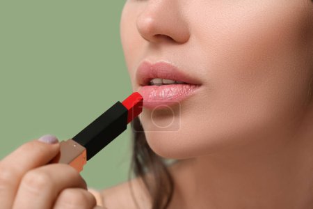 Schöne junge Frau, die roten Lippenstift auf grünem Hintergrund aufträgt, Nahaufnahme