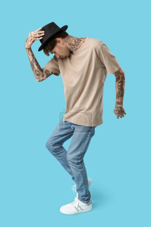Young tattooed man dancing against blue background