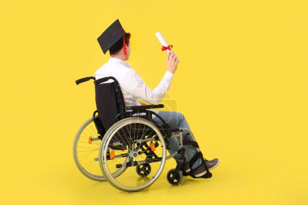 Male graduate in wheelchair with diploma on yellow background
