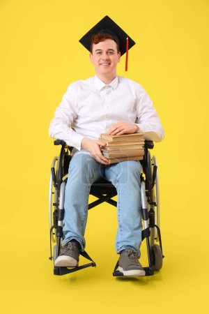 Male graduate in wheelchair with books on yellow background